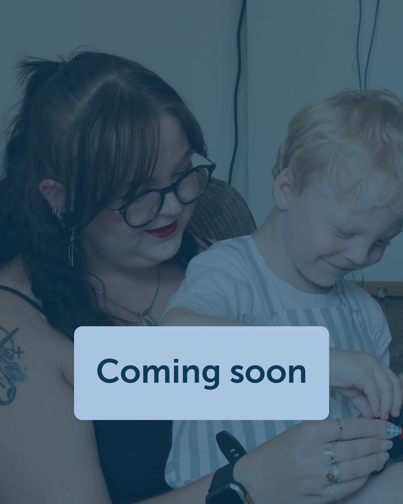 A woman and her son are sat down on a sofa, they both are smiling and playing with a toy.