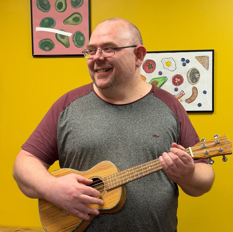 A man wearing a grey and maroon shirt holding a musical instrument.